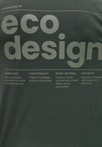 Temna zelena majica s printanim belim besedilom, ki opisuje načela ekološkega oblikovanja, vključno z minimalizmom, funkcionalnostjo in trajnostjo.