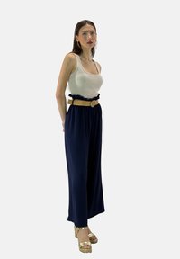 Lichtgrijze tanktop gecombineerd met navy wijde broek en een beige rimpelriem. Gouden haksandalen verhogen de elegantie van de outfit.