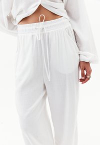 Witte, lichtgewicht, loszittende broek met een elastische tailleband en trekkoord. Geanimeerde stof met zijzakken. Eenvoudig ontwerp.