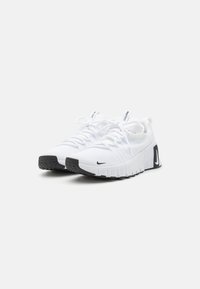 White athletic shoes with a textured mesh upper, lace closure, and a black rubber outsole. Notable Nike branding on the side and heel.