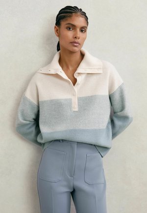 Heledat värvi kudumiskampsun, millel on kreemjad, helesinised ja pehmed hallid horisontaalsed triibud; kraega ja nööbiga esitasku; kombineeritud helesiniste pükstega.