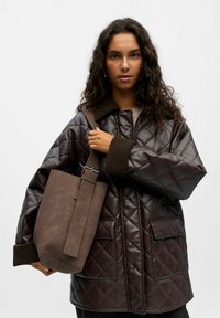 Veste matelassée marron avec un col montant et des poignets côtelés, associée à un sac à épaule en suède marron avec une boucle en métal et une bandoulière réglable.