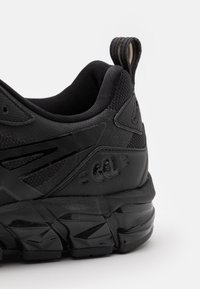 Scarpa sportiva nera caratterizzata da una tomaia testurizzata in materiali mesh e sintetici. Suola spessa e ammortizzata con un distintivo motivo di battistrada e logo.