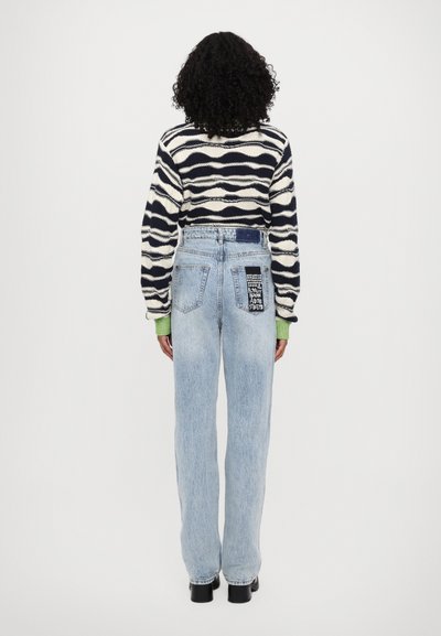 Maglione lavorato a maglia con motivo ondulato blu navy e crema, abbinato a jeans a vita alta di un blu chiaro con tasca a toppa e dettagli grafici.