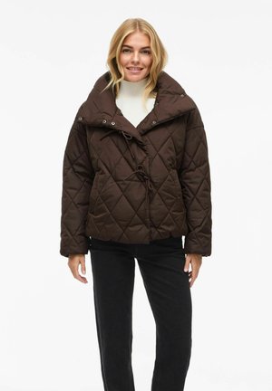 Veste matelassée brune avec un grand col et une taille ajustable par cordon. Elle possède des boutons-pression et une silhouette carrée, associée à un pantalon noir.