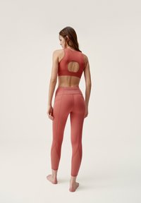 Rostfärgad sport-bh med rund skärning på ryggen, tillsammans med matchande hög midja leggings som har texturerade detaljer på benen.