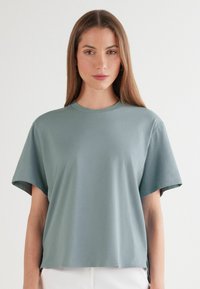 Světlá modrozelená, krátký rukáv tričko vyrobené z měkké látky. Má kulatý výstřih a boční rozparek na lemu pro snadnější pohyb.