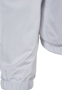 Tessuto bianco con polsini elasticizzati, probabilmente le maniche di una giacca o di un cappotto, mostrato con leggere pieghe e una texture liscia.