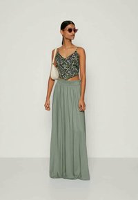 Λουλουδάτο crop τοπ με λεπτές τιράντες, φορεμένο με μια μακριά, ρέουσα, πλισέ ελαιόλευκη μάξι φούστα. Συνοδεύεται από μια μικρή άσπρη τσάντα και γυαλιά ηλίου.