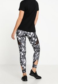 Leggings de patrón en blanco y negro con recortes de malla en los muslos, acompañados de una camiseta negra de manga corta y zapatillas deportivas negras.