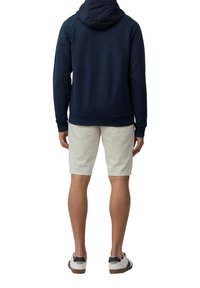 Felpa navy con cappuccio regolabile, abbinata a pantaloni corti beige chiaro. Le scarpe sono bianche con accenti neri e suole marroni.