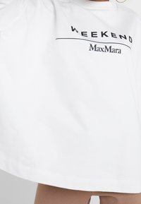 Camiseta de algodón blanca con un logo negro impreso que dice "WEEKEND" y "MaxMara", con un corte suelto y relajado y escote redondo.