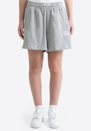 Jambes portant un short Lonsdale gris clair avec une ceinture élastique et des baskets blanches avec des chaussettes courtes sur un fond blanc uni.