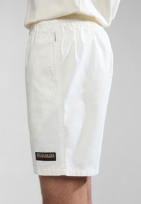 Witte shorts van lichtgewicht materiaal met een elastische tailleband. Zijzakken, met een logo-opdruk op de onderrand. Glad textuur.