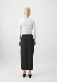 Fehér, hosszú ujjas, bordázott crop top, amelyet magas derekú, bő szárú fekete nadrággal párosítottak. Az öltözék minimalista dizájnnal és elegáns sziluettel rendelkezik.