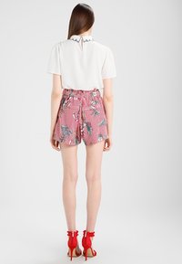 Chemise blanche à manches courtes avec un col à volants, associée à un short à rayures rouges orné de motifs floraux. Chaussures à talons hauts rouges avec des volants.