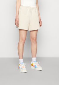 Beige bomullsshorts med resårmidja, i kombination med färgglada sneakers med blå, gula och röda detaljer. Vita ankelsockor syns.