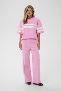 Ružový oversize tričko s bielymi pruhmi, v kombinácii s voľnými ružovými nohavicami so bočnými panelmi. Hladká tkanina a športový štýl.
