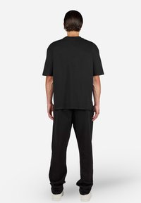 T-shirt noir à manches courtes avec une coupe décontractée, associé à un pantalon noir ample et des baskets de couleur claire, avec peu de texture et de détails de design.