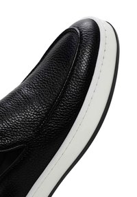 Black leather slip-on shoe with textured upper, white midsole, and contrasting stitching detail along the edge. Rounded toe design.