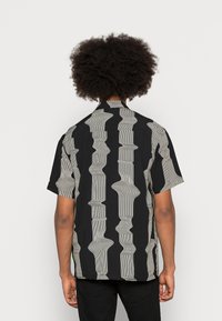 Camicia a maniche corte in tessuto nero con motivo a righe ondulate bianche a contrasto, con vestibilità rilassata e colletto standard.