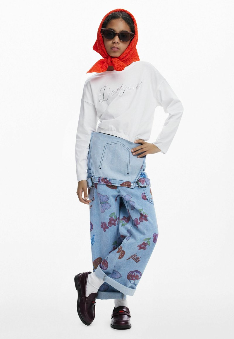 Weißes Langarmhemd mit Strassschriftzug, hellblaue Jeans-Shorts mit Blumenmuster, roter Schal und dunkle Sonnenbrille. Braune Schuhe mit Socken.