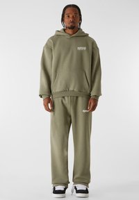 Olivgrüner Hoodie und passende Jogginghose aus weichem Material, mit einer Fronttasche und Logodetail, im lässigen Schnitt und mit Bündchen an den Knöcheln.