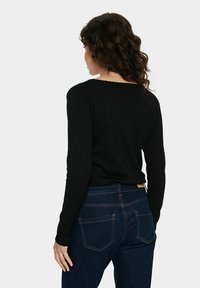 Fekete, hosszú ujjú felső, fodros dekoltázzsal, sötét farmernadrággal párosítva, amely kontrasztos varrással és két hátsó zsebbel rendelkezik.