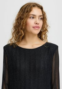 Top negru cu guler rotund, maneci lungi transparente și dungi metalice verticale pentru textură și model. Finisaj de țesătură netedă.