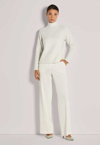 Weißer gerippter Strick-Turtleneck-Pullover kombiniert mit weit geschnittenen Hosen, beide mit einer weichen Textur und entspanntem Schnitt. Neutrale Farbe und minimalistisches Design.