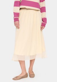 Crème-kleurige, vloeiende midi-rok met een transparante onderlaag. Gepaard met beige, met stippen bedrukte flats. Eenvoudig ontwerp met elastische tailleband.