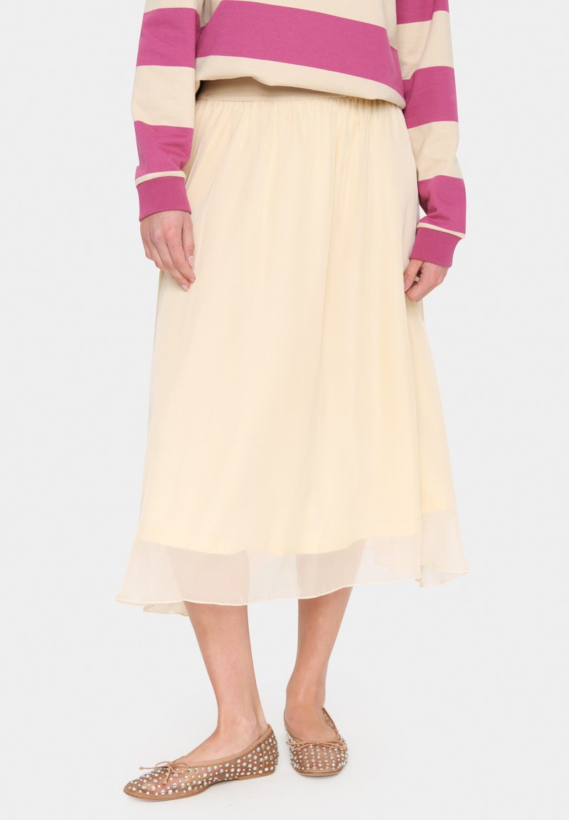 Crème-kleurige, vloeiende midi-rok met een transparante onderlaag. Gepaard met beige, met stippen bedrukte flats. Eenvoudig ontwerp met elastische tailleband.