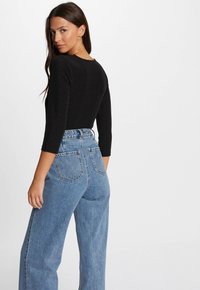 Schwarzer Langarm-Body mit Rundhalsausschnitt, kombiniert mit hochtaillierten, hellblauen Jeans aus Denim mit zwei hinteren Taschen und lockerer Passform.