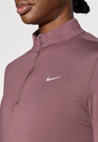 Ζιπ-απ μπλούζα Nike σε αποχρώσεις απαλού μωβ ύφασματος, με ψηλό γιακά, μερικό φερμουάρ και μικρό λευκό λογότυπο στο στήθος. Ομαλή υφή.