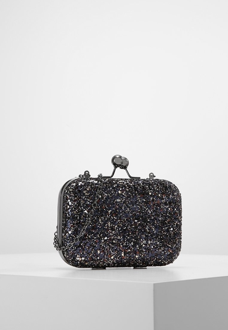 Petit sac pochette rectangulaire noir pailleté avec fermoir kiss-lock en métal et anse chaîne assortie sur surface blanche.