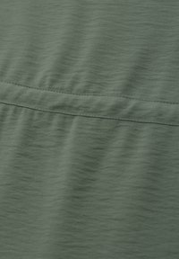 Gros plan d'un tissu vert olive avec une couture horizontale et un motif tissé subtilement texturé.