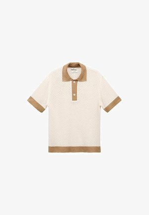 Lyhythihainen polo-paita, jossa on kermaista rei'itettyä kangasta ja ruskeita yksityiskohtia kauluksessa ja helmassa, esittelee kaksiknappista etulukkoa.