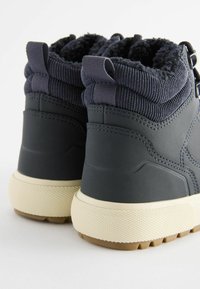 Vue arrière de bottes d'hiver noires avec collets matelassés côtelés, languettes de traction, semelles blanches texturées et semelles extérieures brun foncé à rainures.