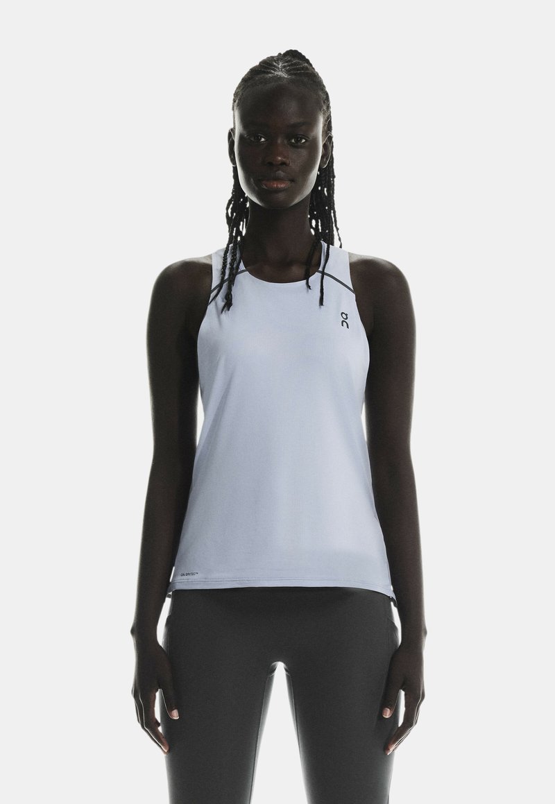Canotta atletica di colore azzurro chiaro con una texture liscia, design racerback e un piccolo logo sul lato sinistro del petto. Indossata con leggings neri.