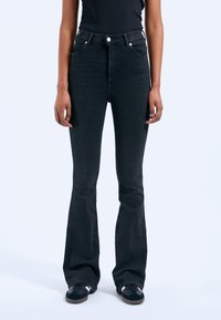 Black flared jeans with five pockets, button closure, and a smooth texture. Pairing with black sneakers completes the look.