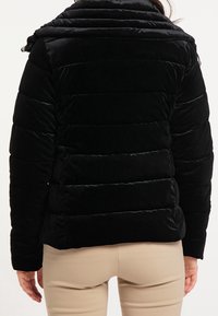 Svart sammet puffjacka med horisontella sömmar, hög krage och dragsko vid halsen. Mjuk textur och slim-fit design.