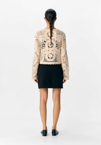 Crocheterad beige tröja med långa ärmar, med intrikata mönster. Kombinerad med en figurnära svart kjol och svarta platta skor.