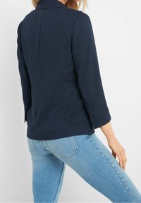 Marineblaues Blazer mit strukturiertem Kragen, Dreiviertelärmeln und glatter Oberfläche, kombiniert mit hellblauen Slim-Fit-Jeans.