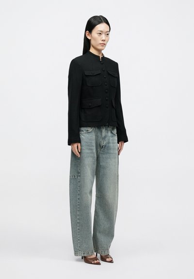 Sort figursyet jakke med fire forlommer og knaplukning, kombineret med lyseblå løstsiddende jeans og brune sandaler med hæl.