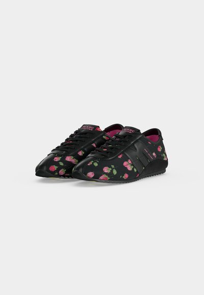 Paire de baskets noires avec motifs de roses roses, lacets noirs et doublure intérieure rose placée sur un fond gris clair uni.