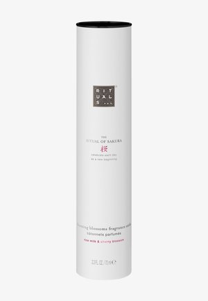 Conteneur cylindrique blanc avec un couvercle noir, portant un logo argenté et un texte rose. Contient des bâtons parfumés à la senteur de lait de riz et de fleur de cerisier.