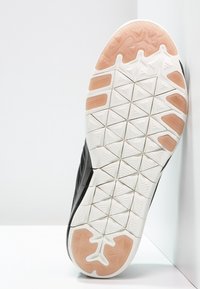 Musta urheilujalkineen pohja, jossa on tekstuuroitu kuminen muotoilu, jossa on kolmikulmaisia kuvioita ja oransseja yksityiskohtia. Matala-profiilinen, joustava rakenne.