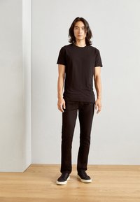 T-shirt noir à manches courtes, design ajusté, associé à un pantalon noir à jambes droites et des baskets noires avec semelles blanches ; texture de tissu lisse.