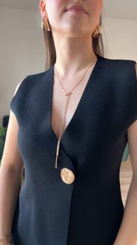 Top senza maniche nero con texture, caratterizzato da un colletto a V, un grande bottone dorato e una collana dorata a più strati con pendente e dettagli a catena.