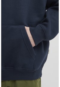 Námornícky modrá mikina vyrobená z jemnej bavlnenej zmesi, so prednou kapsou, rebrovanými manžetami a lemom. Hladká textúra s voľným strihom.